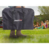 A large dark gray Royal Gourmet storage bag being carried by a person outdoors on a grassy lawn, with a blurred background of people sitting on the grass.