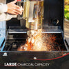 Person using a chimney starter to light charcoal in a Royal Gourmet grill with sparks flying.
