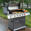 A stainless steel outdoor Royal Gourmet gas grill with a lid, side shelf, and three front control knobs, shown cooking food on a wooden deck with grass and trees in the background.