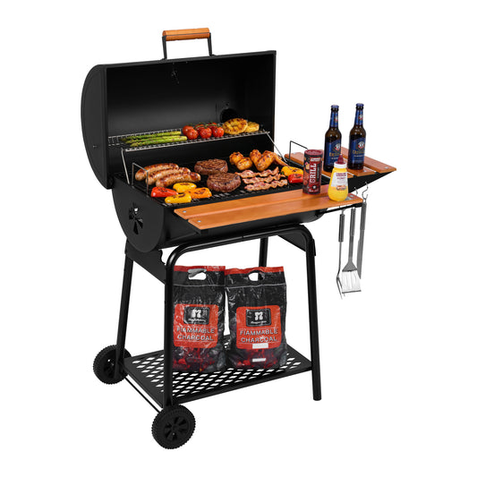 A black Royal Gourmet charcoal grill with an open lid, wooden side table, and wheels, shown loaded with food, bottles, utensils, and two bags of Royal Gourmet charcoal on a white background.