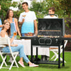 Group of people enjoying a barbecue outdoors with a grill in the foreground.