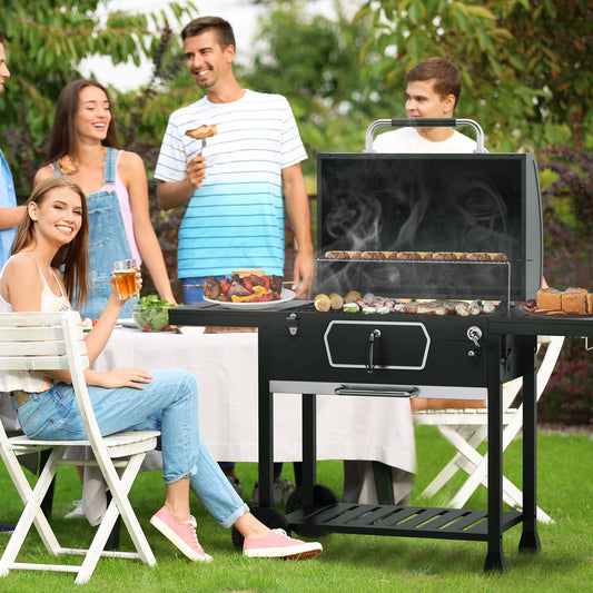 Group of people enjoying a barbecue outdoors with a grill in the foreground.