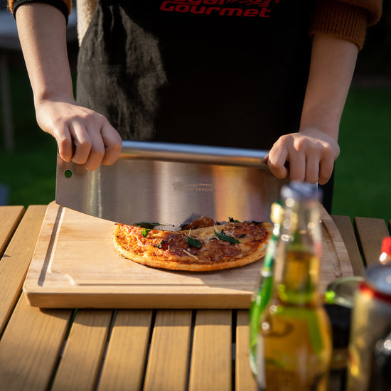 Person cutting a pizza on a wooden board with a beer bottle and can in the background