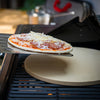 Uncooked pizza being placed on a grill with a Royal Gourmet pizza stone.