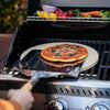 Person using a Royal Gourmet pizza peel to place a pizza on a grill with vegetables.