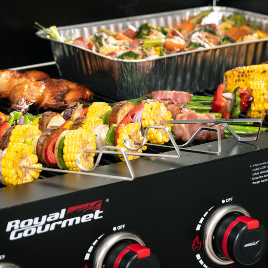 Royal Gourmet  Grill with skewers of vegetables and meats, and a tray of food in the background.