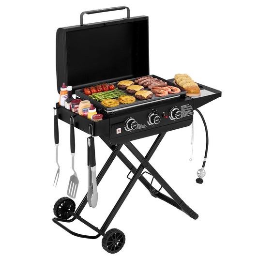 A black portable folding Royal Gourmet gas grill with wheels, shown open with food cooking on the griddle and side tray. The grill has two control knobs, hanging utensil holders with tongs and spatulas, and a clean white studio background.